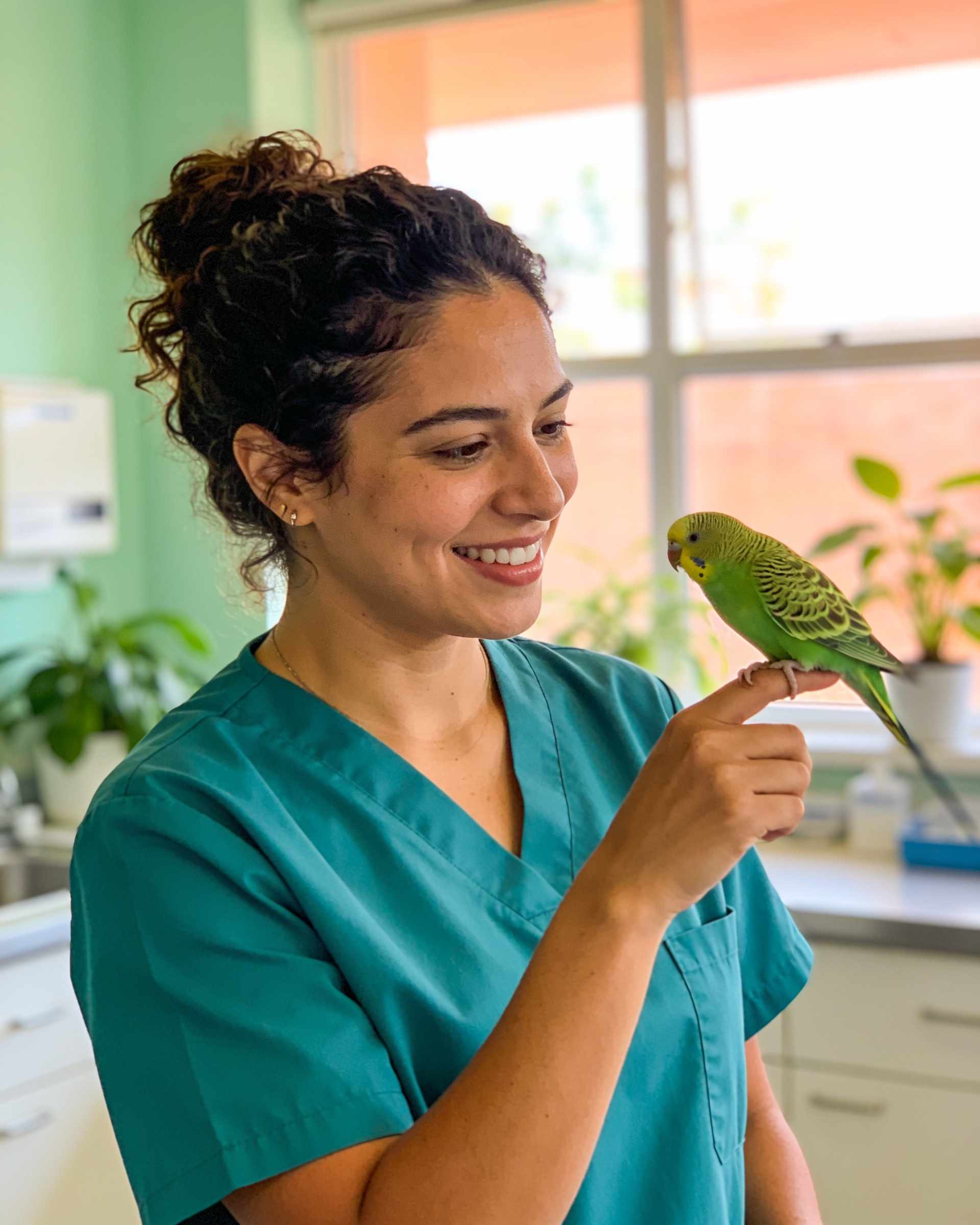 Portrait of a cheerful vet with dark curly hair in teal scrubs, a green parakeet on her finger.